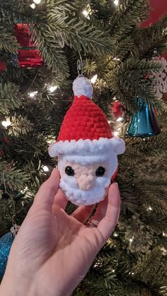 someone is holding up a tiny santa clause ornament in front of a christmas tree