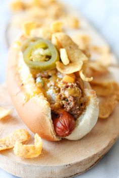 a hot dog with toppings and chips on a cutting board