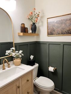 a white toilet sitting next to a sink in a bathroom under a framed painting on the wall