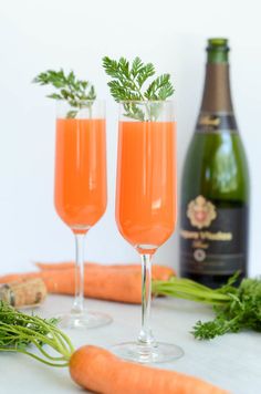 two wine glasses filled with carrot juice and garnished with parsley next to a bottle of champagne