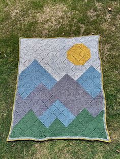 a crocheted blanket sitting on top of a green grass covered field next to a yellow ball