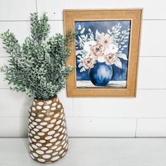 a vase filled with flowers sitting on top of a table next to a framed painting