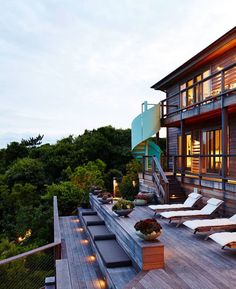 an outdoor deck with chaise lounges and lights on the side of the house