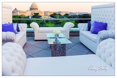 a living room filled with white couches and chairs next to a glass table on top of a roof