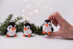 three small crocheted penguins sitting on top of a white table next to a christmas tree