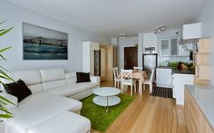 a living room filled with white furniture next to a kitchen and dining room table on top of a hard wood floor