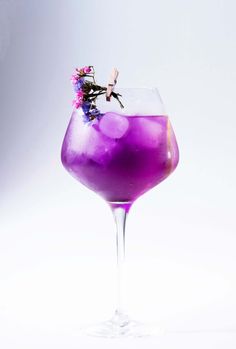 a purple drink in a wine glass on a white background with some flowers sticking out of the top