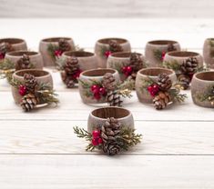 there are many pine cones and red berries in the cup holders on the white table