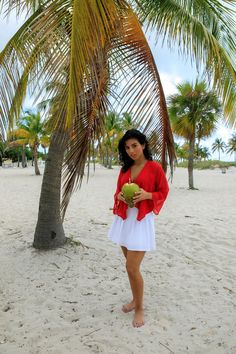 a woman holding a coconut under a palm tree