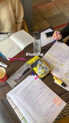 two people are sitting at a table with books and papers on it, one person is holding a pen