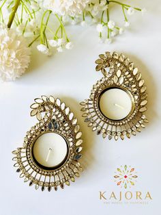 two white candles sitting on top of a table next to flowers