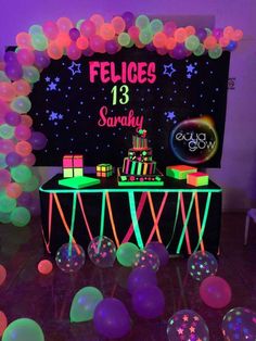 a table topped with lots of balloons and cake on top of a table covered in neon lights