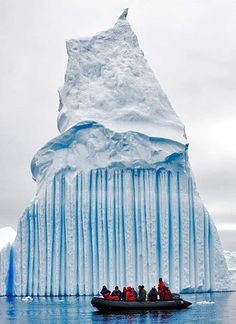 an iceberg with several people in a raft on the water next to it's surface