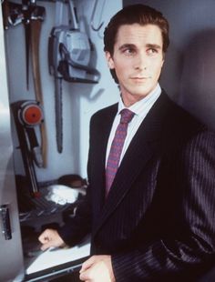 a man in a suit and tie standing next to a desk with a computer on it