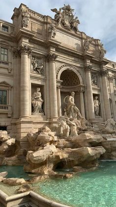 an ornate building with statues on the front and sides next to a pool of water