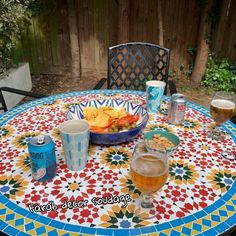 a colorful table with drinks and food on it in a backyard setting, next to a wooden fence