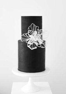 a black and white wedding cake with a flower on the top is sitting on a pedestal