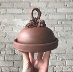 a hand holding a chocolate covered dish in front of a brick wall with a flower decoration on it