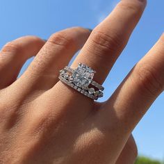 a woman's hand with a diamond ring on top of her finger and the sky in the background