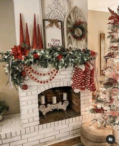 a decorated christmas tree sitting in front of a white brick fireplace with red and green decorations