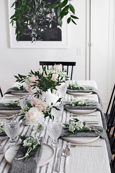 the table is set with white and black plates, silverware, and floral centerpieces