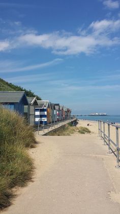 the beach is lined with small huts and grass on either side of the path to the water's edge