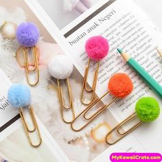 four different colored pom - pom clips on top of a book with a pen