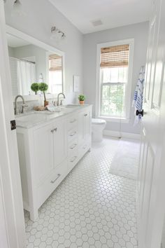 a white bathroom with hexagonal tile flooring and window above the toilet area