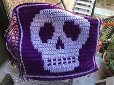 a crocheted bag with a skull on the front and purple trim around it