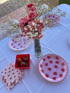 the table is set with pink plates, flowers and strawberries in vases on it