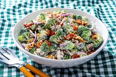 a white bowl filled with broccoli salad next to two orange handled utensils