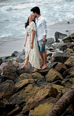 a man and woman kissing on the rocks by the ocean with waves in the background