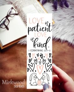 someone holding up a bookmark with the words love is patient love, and two hearts