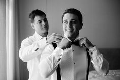 two men in white shirts and black ties are fixing their bowties on the same shirt