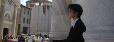 a man in a suit and tie standing next to a column with people walking around