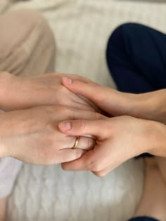 two hands holding each other on top of a white couch with pillows in the background