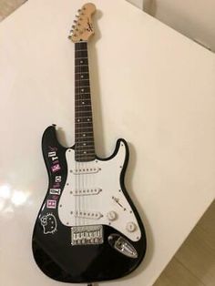 a black and white electric guitar on top of a table next to a wall with writing on it