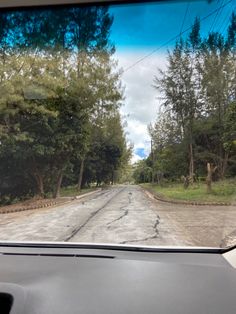 the view from inside a car looking down an empty road with trees on both sides