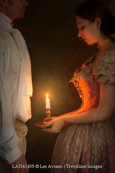 a man and woman standing next to each other holding a lit candle in their hands