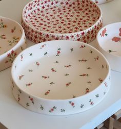 three white bowls with red flowers on them sitting on a table next to each other