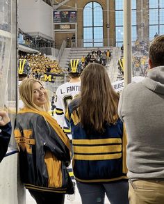 two women and one man standing in front of an ice hockey rink with fans looking on