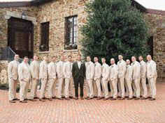 a group of men standing next to each other in front of a brick building with trees