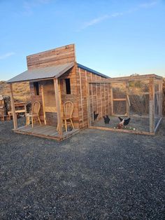 a chicken coop in the middle of a gravel lot with chairs and chickens on it