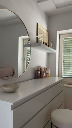 a white bathroom with a round mirror above the vanity and stools in front of it