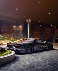 a black sports car is parked in front of a building with flowers and plants around it