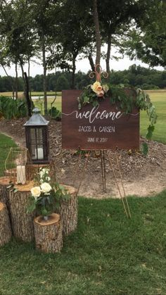 a welcome sign and tree stumps in front of a grassy area with flowers on it