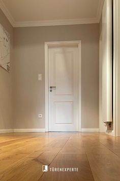 an empty room with a white door and hard wood flooring on either side of it