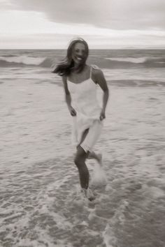 black and white photograph of woman running in the water at the beach with her hair blowing in the wind