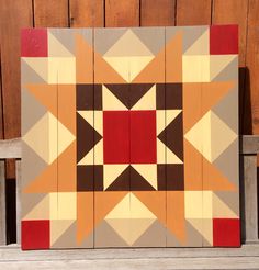 a wooden block with an orange, brown and red star design on the front is sitting on a bench