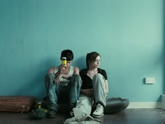 two people sitting on the floor in front of a blue wall